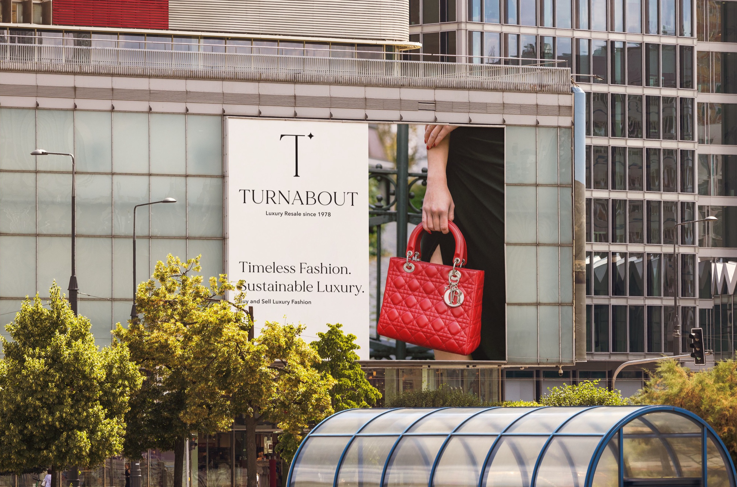 A large building billboard reading ‘Timeless Fashion. Sustainable Luxury.’ beside a red designer handbag.