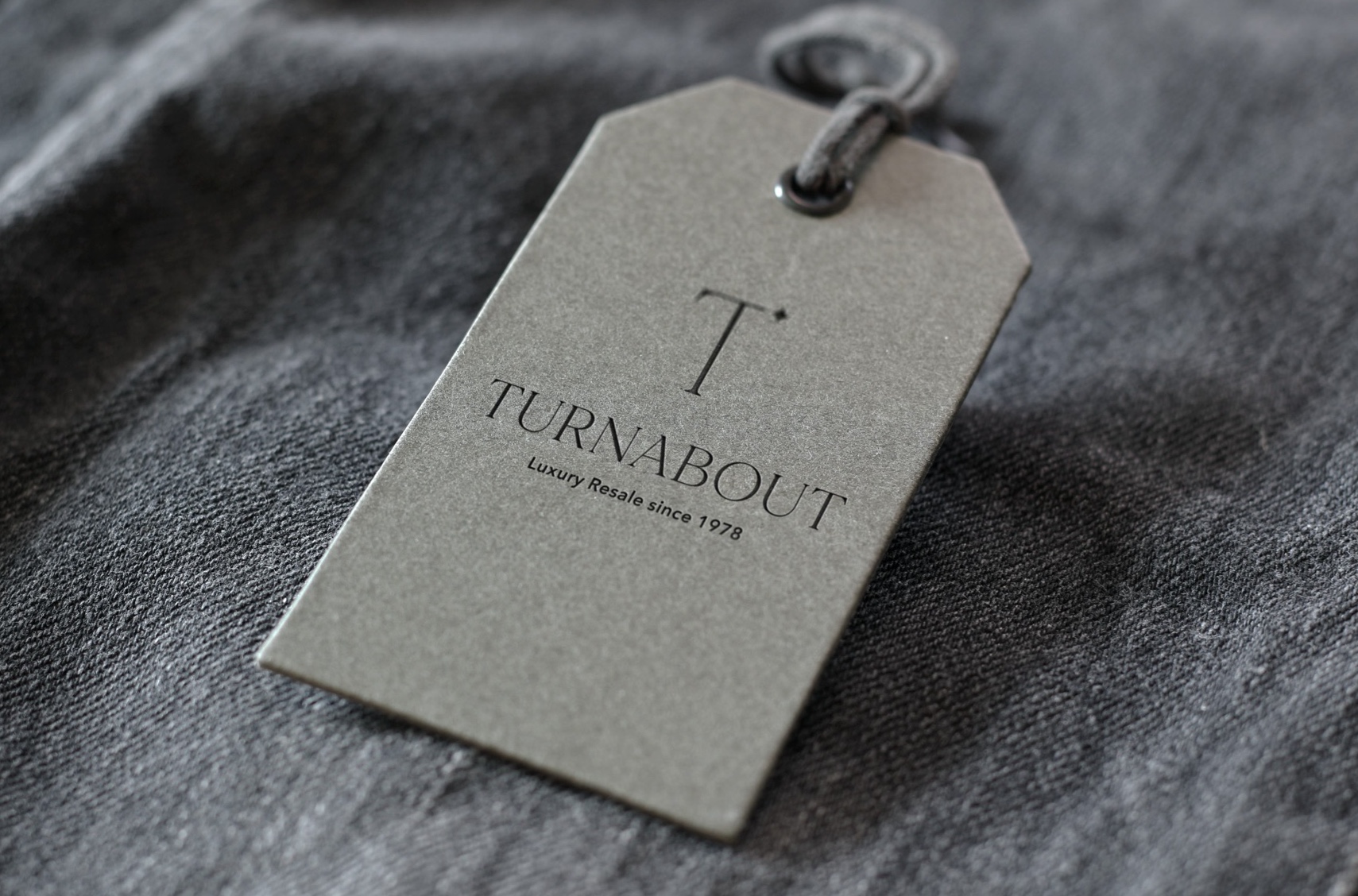 A grey hang tag with the Turnabout logo and ‘Luxury Resale since 1978’ resting on dark denim.