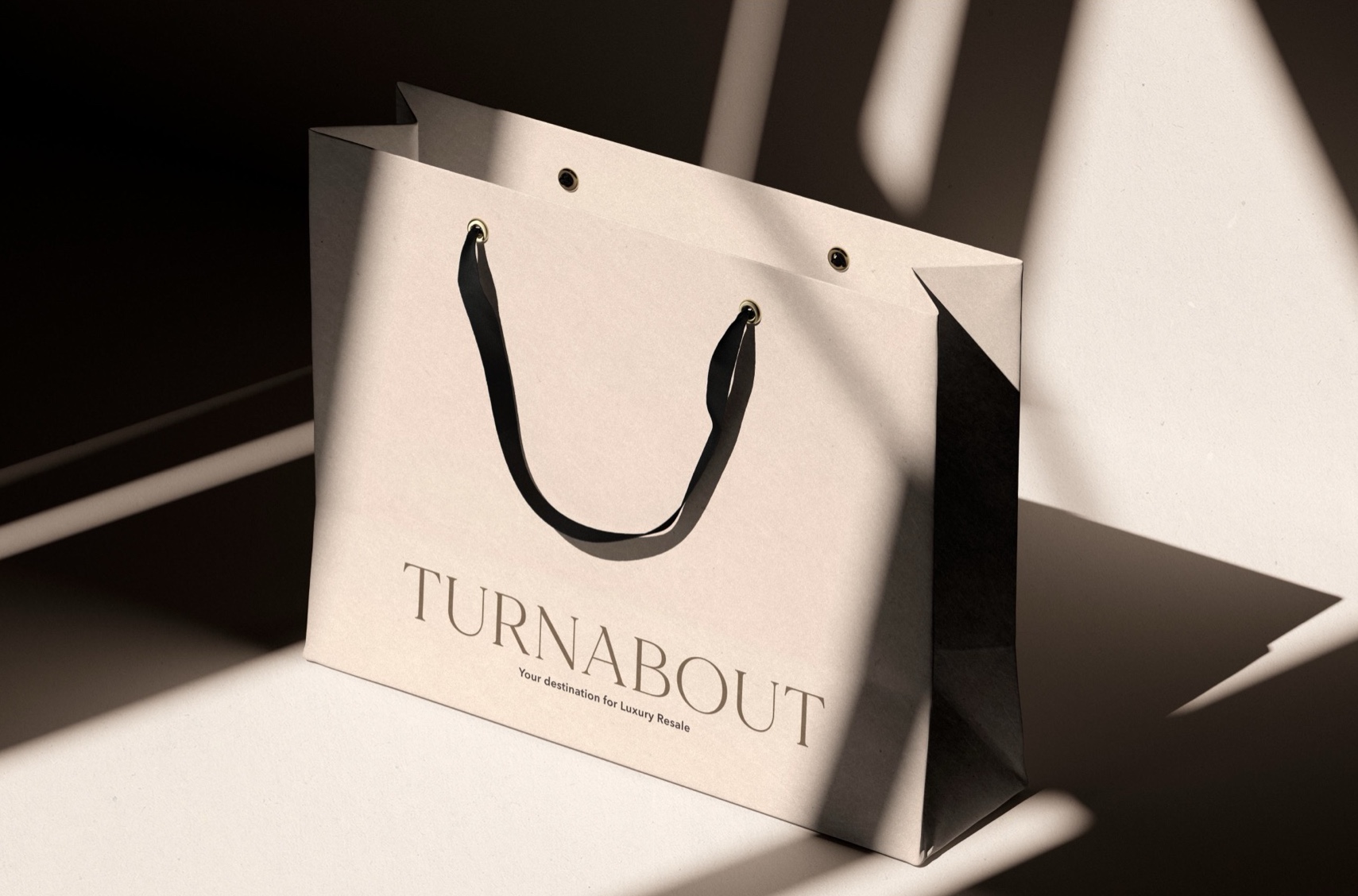 A Moon Mist shopping bag with black handles, printed with the Turnabout wordmark and ‘Your destination for Luxury Resale’.